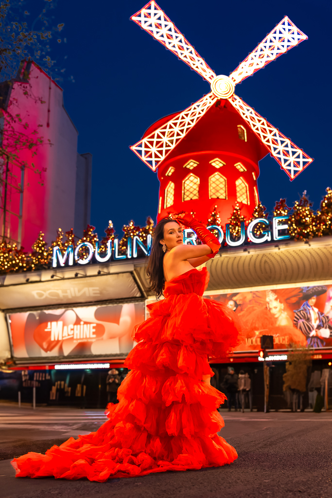 Woman in a red fluffy gown posing in front of Moulin Rouge at night