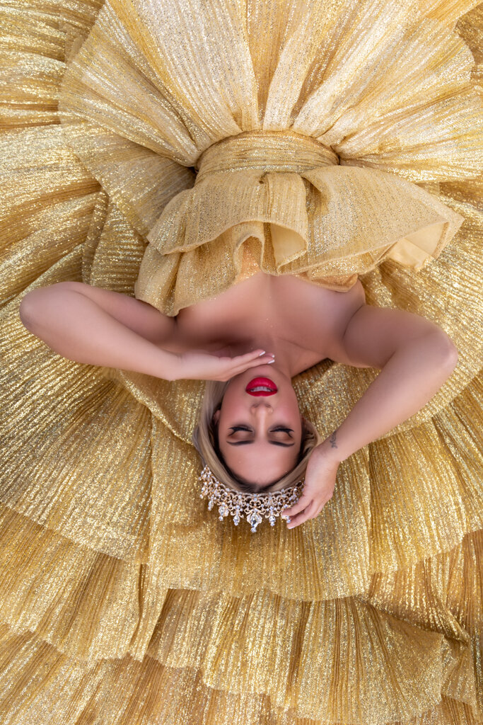 Close-up portrait of a woman lying on a gold gown wearing a tiara