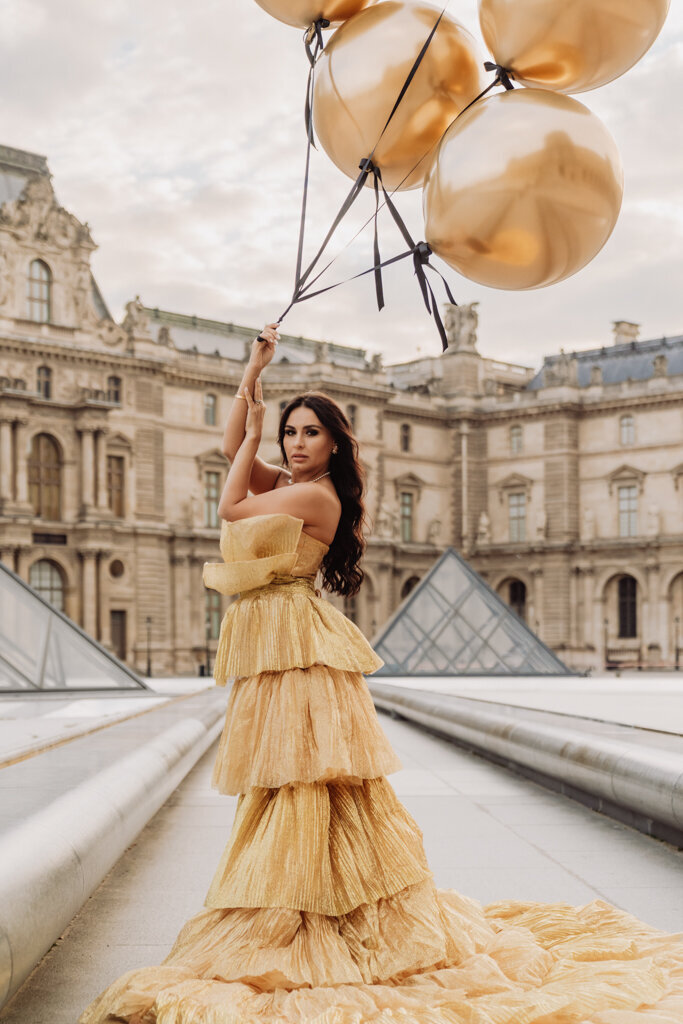 Woman in a gold gown with golden balloons at the Louvre courtyard in Paris