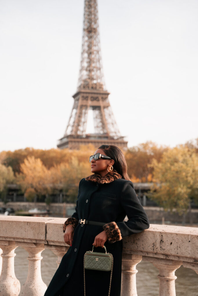 Fall photoshoot in Paris with Eiffel Tower view, woman in a black coat on a bridge